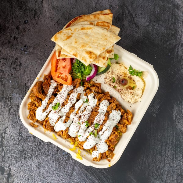 Chicken shawarma plate with rice, pita bread, hummus, and salad, drizzled with white sauce.