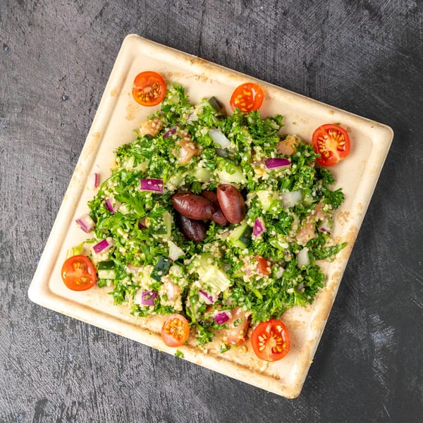 Tabbouleh salad with parsley, bulgur, tomatoes, cucumbers, red onions, and olives on a rectangular plate.