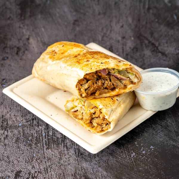 Two halves of a chicken shawarma wrap with red onions and pickles, served with a side of white sauce.