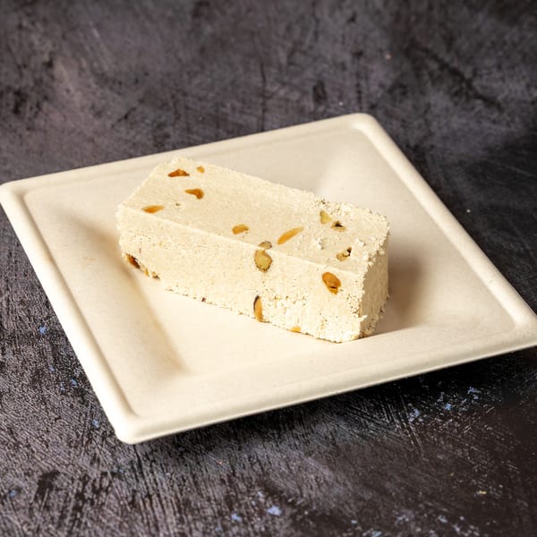 A rectangular piece of light-colored halva with nuts on a cream-colored plate.