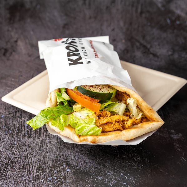 A Kronos gyros with chicken, lettuce, tomato, and cucumber on a beige tray.