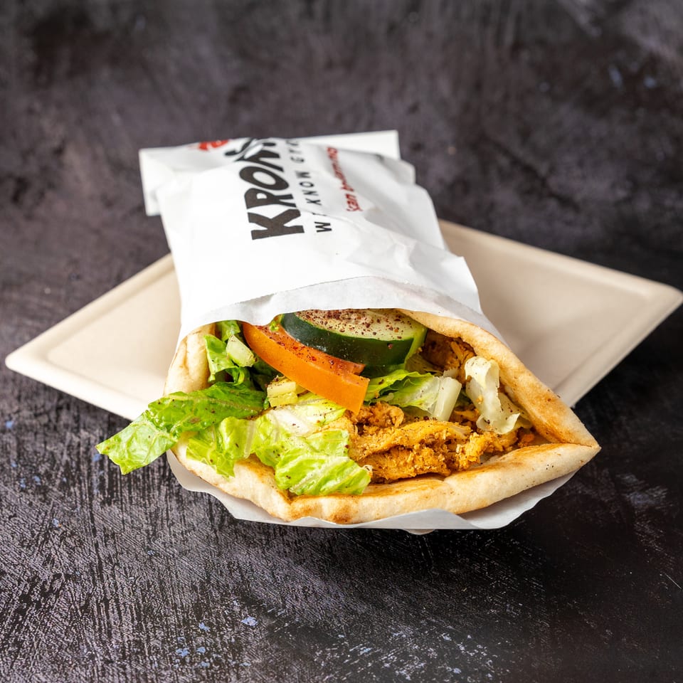 A Kronos gyros with chicken, lettuce, tomato, and cucumber on a beige tray.